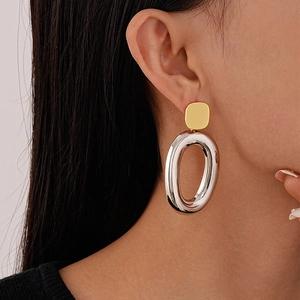 Close-up of minimalist geometric gold stud and large oval silver metal drop earrings