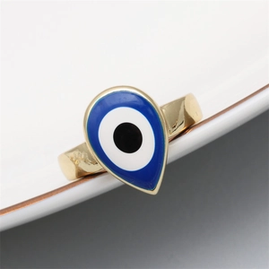 Detail of a golden water-drop evil eye ring with blue enamel on a white ceramic plate