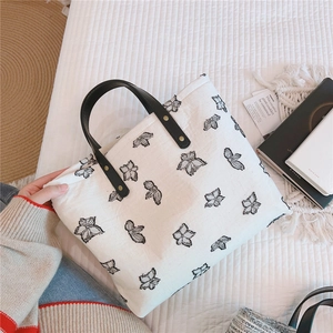 Détail du sac cabas en toile blanche à motifs noirs et anses en cuir à rivets dorés