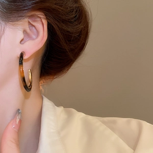 Detailed close-up of vintage resin C-shape hoop earrings worn on a model's ear lobe