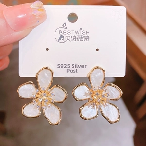 Macro shot of five-petal flower earrings with white resin inlay and zircon center on card