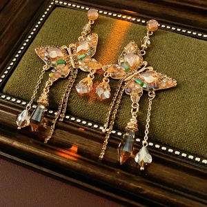 Gros plan de boucles d'oreilles papillon à pompons avec cristaux champagne sur velours