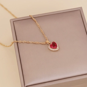 Elegant gold necklace with red heart gemstone and zircon halo on champagne box