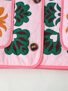 Detail of pink cotton jacket featuring green wave print and brown marble texture button