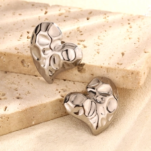 Macro detail of silver heart earrings with a hammered texture and polished finish