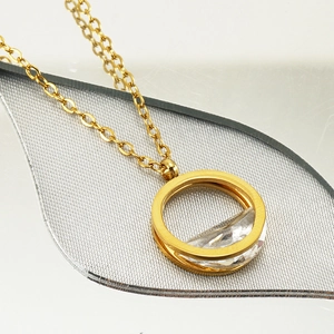 Détail d'un collier doré rond avec cristal transparent sur une surface réfléchissante