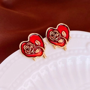 Macro detail of vintage gold heart earrings with red enamel and embossed rose patterns