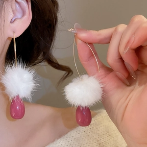 Dettaglio di orecchini a goccia con pompon bianco e ciondolo a goccia rosso su ganci dorati