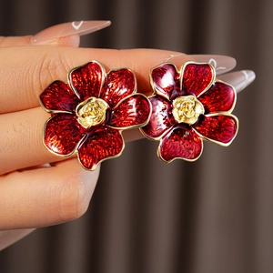 Primer plano de pendientes de flores rojas vintage con borde dorado sostenidos por una mano
