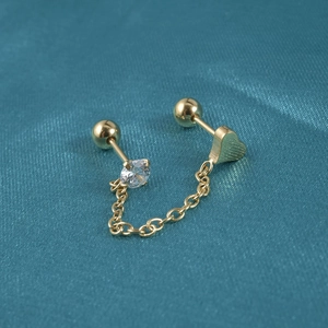 Detailed shot of golden chain stud earrings with heart charm and zircon on silk fabric