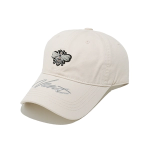 Macro detail of bee embroidery and cursive script on cream cotton baseball cap