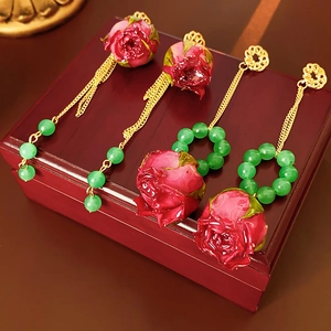 Makroaufnahme von rosa Rosenquasten-Ohrringen mit Goldketten auf dunklem Holz