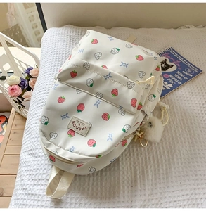 Detailed view of white strawberry backpack with heart prints and soft pompom charm