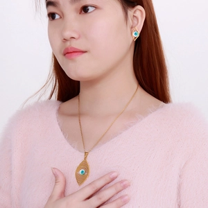 Detail of bohemian gold evil eye necklace and earrings set worn with a pink sweater