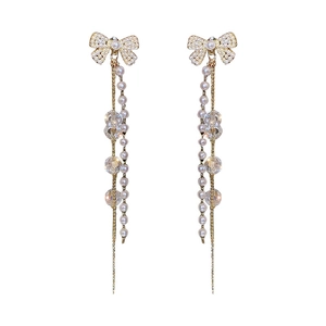 Élégantes boucles d'oreilles nœud dorées avec perles blanches et longs pompons en cristal