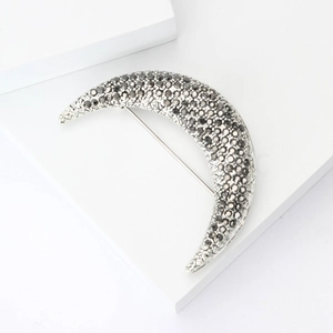 Elegant crescent moon brooch with dark crystal pavé on white geometric display stand