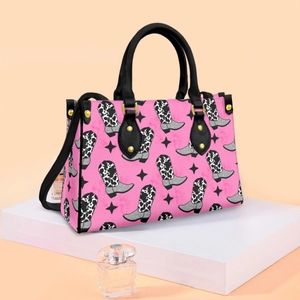Pink tote bag with cow print cowboy boots pattern, black handles and gold hardware accents