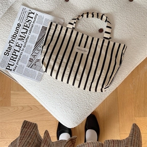 Close-up of black and white striped canvas tote bag on textured white cushion with newspaper