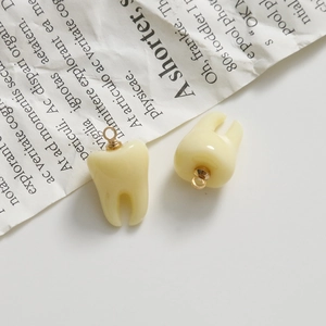 Macro shot of 3D resin tooth pendants in cream white with gold metal hanging loops