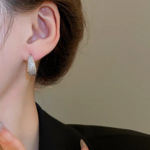 Close-up of silver U-shaped huggie earrings with cubic zirconia on female model ear