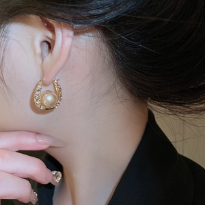Close-up of sparkling horseshoe earrings with champagne pearls on female model