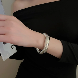 Close-up of minimalist silver wavy bangle with polished mirror finish on model's wrist