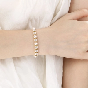 Détail du bracelet élégant avec perles blanches et perles en métal doré au poignet