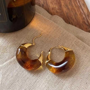 Close-up of amber resin C-shaped hoop earrings with gold metal clasp on beige fabric