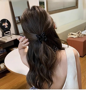 Detail showing an elegant black satin bow hair claw clip styled on long wavy hair