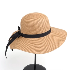 Detail of wide brim straw sun hat featuring a black ribbon bow on a white background