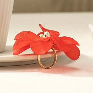 Red acrylic flower ring with white pearls and gold metal band for women on white porcelain
