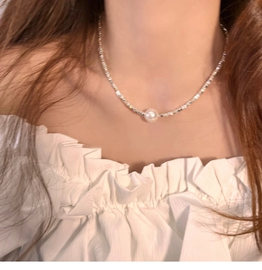 Detail of a square crushed silver chain necklace featuring a single white pearl on a model