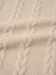Detailed macro shot of beige knit sweater texture showing cable and honeycomb patterns