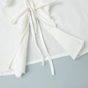 Detailed macro view of white cotton shirt featuring neck ties and delicate ruffle edges