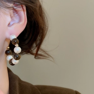 Détail de créoles en C avec perles blanches et œil de tigre marron portées à l'oreille