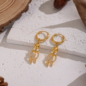 Details von goldenen Oktopus-Ohrringen mit Zirkonia auf rustikalem Hintergrund im Naturstil