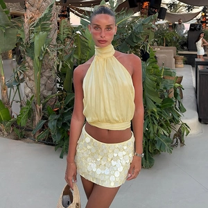 Detail of yellow halter top and sequined mini skirt on model in tropical setting