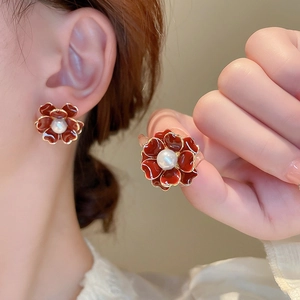 Détail de boucles d'oreilles fleur rouge avec perle blanche et finition dorée élégante