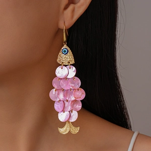 Macro shot of unique golden fish earring with pink shell scales and blue evil eye detail