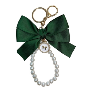 Handmade keychain featuring a large dark green ribbon bow and white pearl bead loop