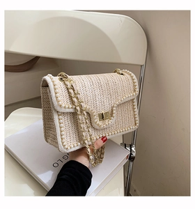 Detail of straw woven crossbody bag with pearl trim and gold chain strap handle