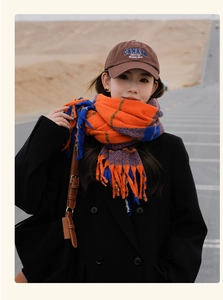 Close-up of orange and blue plaid scarf with tassels and embroidered baseball cap