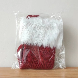 Close-up of a red knitted Christmas stocking with white faux fur cuff in polybag packaging
