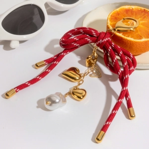 Detail of red woven bow bag charm with gold hearts and baroque pearl on white background