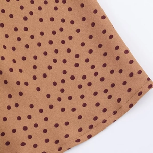 Close-up of brown midi dress fabric with dark red polka dots and fine stitched hemline