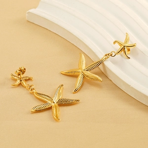 Fashionable gold starfish drop earrings on elegant fabric with a stone background decor