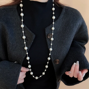 Detail of layered white shell and irregular glass pearl necklace on elegant dark sweater