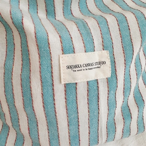 Close-up of blue and white striped canvas fabric with red stitching and woven brand label