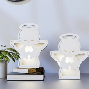 Close-up of white angel wings cutout night light with warm LED glow on a grey surface