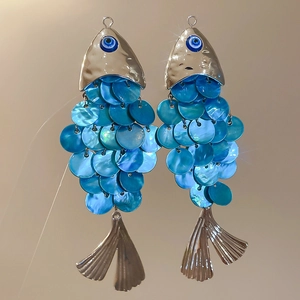 Macro shot of fish-shaped earrings with blue shell scales and blue evil eye beads